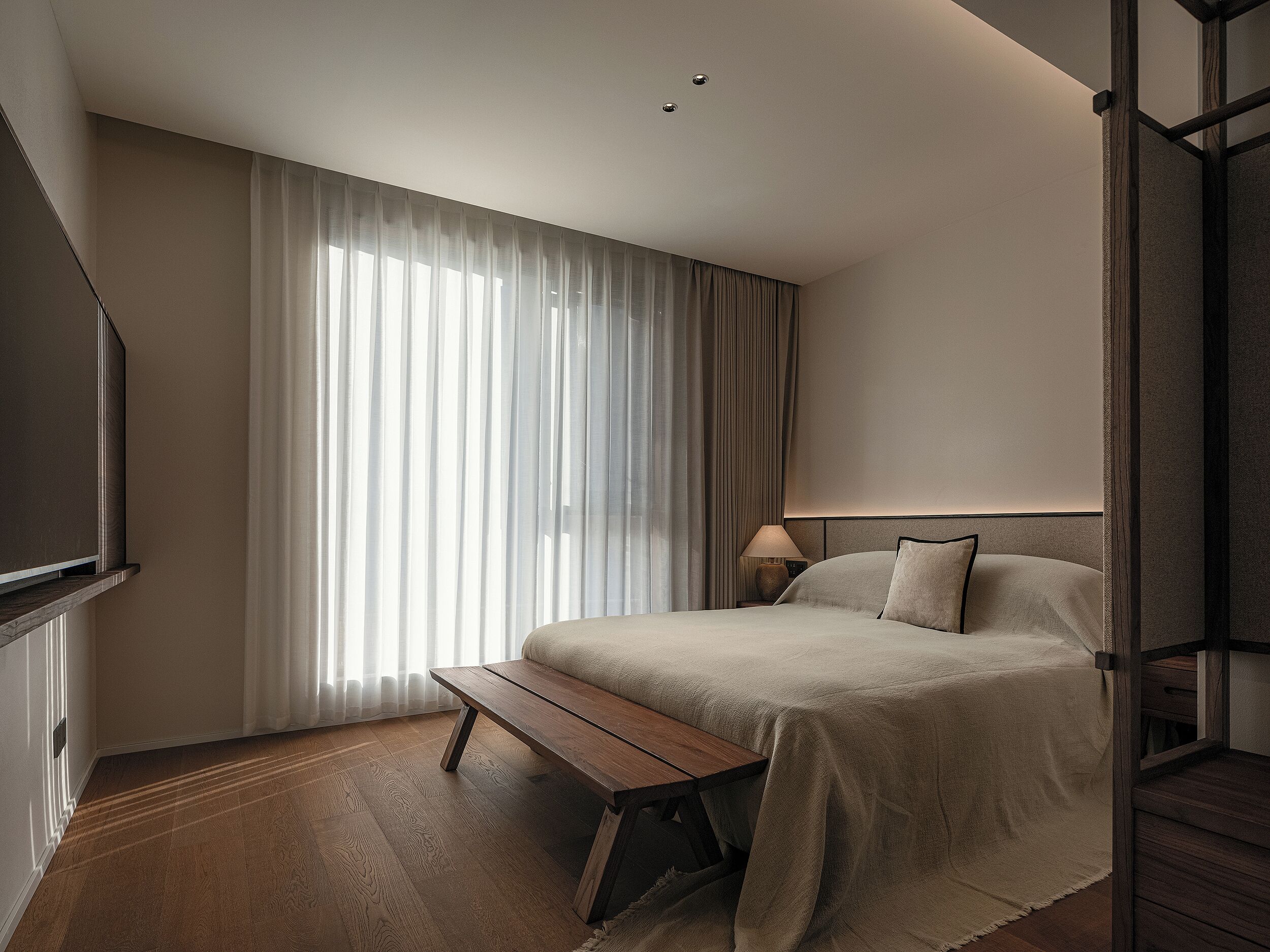 A hotel room with a bed, a bench, a TV, and a lamp.