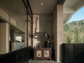 A modern interior with a large window, a decorative tree branch, a cabinet with a picture, and a view of a hillside. - Zhangjiajie national park Oxgen Resort (Zhangjiajie)