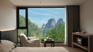 A bedroom with a large window, a bed, a chair, a small table with a cup, and a TV stand. - Zhangjiajie national park Oxgen Resort (Zhangjiajie)