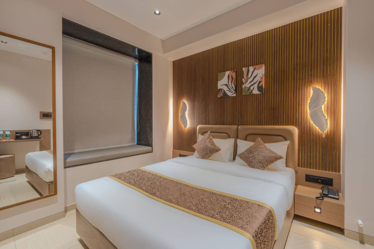 Una habitación de hotel moderna con una cama grande, una mesita de noche con teléfono, un espejo y una ventana con persianas.