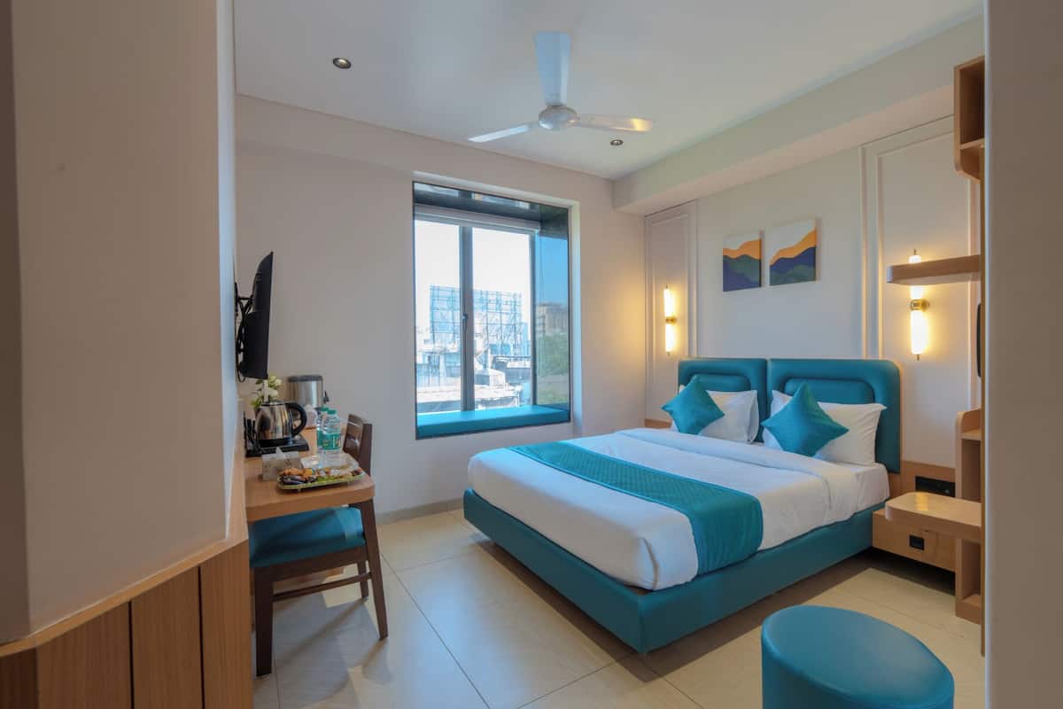 Una habitación de hotel moderna con una cama grande, un escritorio con silla, un ventanal con vista a la ciudad y un ventilador de techo.