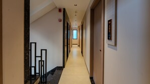 Moderni hotellin käytävä, jossa on marmoriporras, palovaroitin ja seinään asennettu hissin ohjauspaneeli.