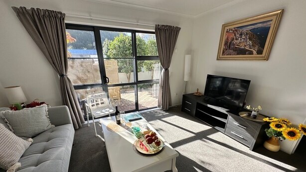 A living room with a sofa, a coffee table with fruit, a TV, and a painting on the wall. - *Quiet, Cozy & Family-Friendly | Pool, Gym, Shops & Transport Nearby (Northshore)