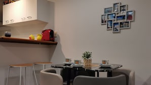 A dining area with a table set for four, two bar stools, a shelf with kitchen items, and a wall with framed pictures. - *Quiet, Cozy & Family-Friendly | Pool, Gym, Shops & Transport Nearby (Northshore)