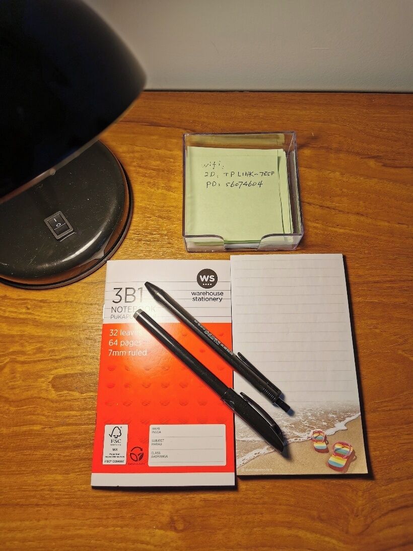 A desk with a notebook, a pen, a sticky note, and a pair of flip-flops.