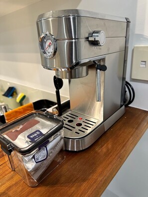 A stainless steel coffee machine with a digital pressure gauge, a water reservoir, and a clear plastic container with a label. - *Quiet, Cozy & Family-Friendly | Pool, Gym, Shops & Transport Nearby (Northshore)