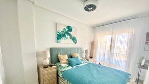 Un dormitorio con cama, mesitas de noche, una obra de arte colgada en la pared y una ventana con cortinas.