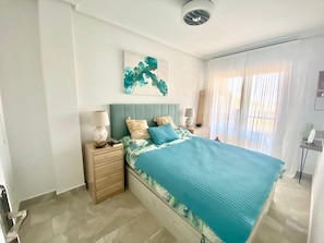Ein Schlafzimmer mit einem Bett, Nachttischen, einem Wandbild und einem Fenster mit Vorhängen.