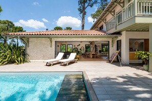 A poolside area with a stone wall, two lounge chairs, a dining table, and a painting easel. - Beautiful villa ideally located with heated pool, 4*, 5 bed, Arcachon (Arcachon)