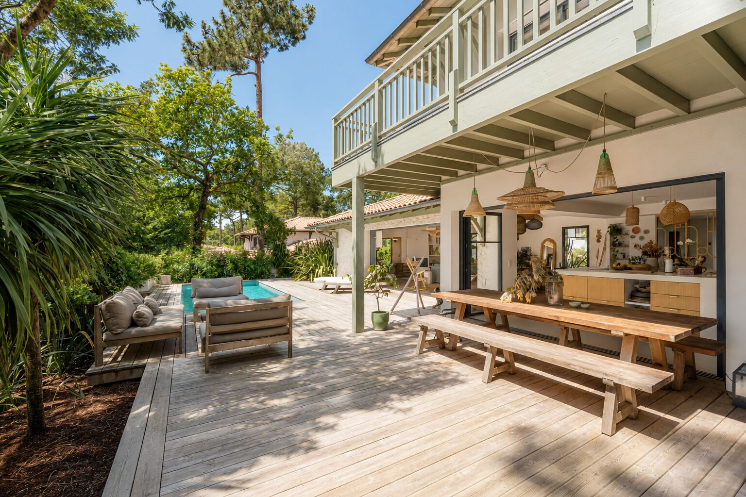 A wooden deck with outdoor furniture, a pool, and a kitchen area with hanging lights.