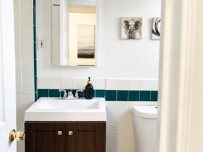 Un baño con lavamanos blanco, armarios de madera oscura, inodoro blanco y azulejos color turquesa.