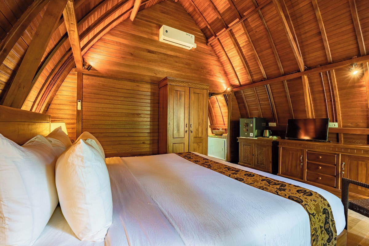 A bedroom with a large bed, wooden ceiling beams, a television, and a kitchen area.