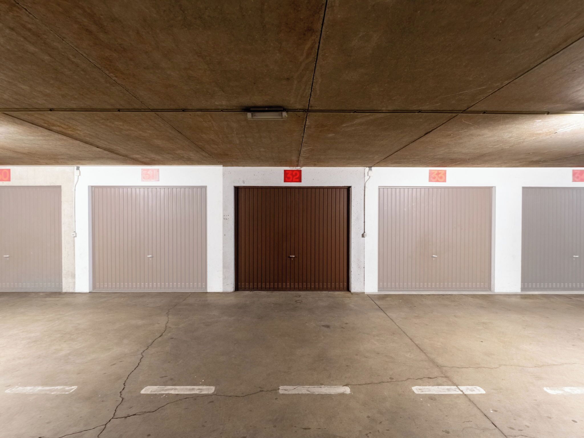 Un parking avec des planchers et des murs en béton, doté d’une porte centrale au-dessus de laquelle est affiché un panneau rouge.