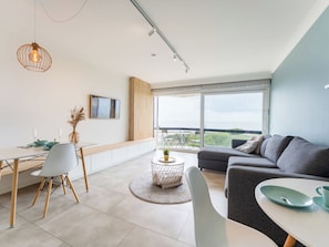 Ein modernes Wohnzimmer mit Sofa, Esstisch, Stühlen, einem großen Fenster mit Aussicht und einer Hängelampe.