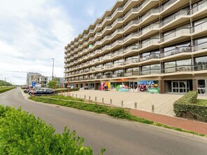 Ein mehrstöckiges Hotel mit Balkonen, einem Parkplatz und einer Ladenfront mit Werbeanzeigen.
