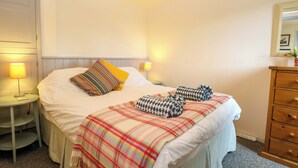 Ein ordentlich bezogenes Bett mit einer Karo-Decke, zwei Kissen und einer Nachttischlampe.