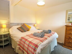 Ein ordentlich bezogenes Bett mit einer Karo-Decke, zwei Kissen und einer Nachttischlampe.