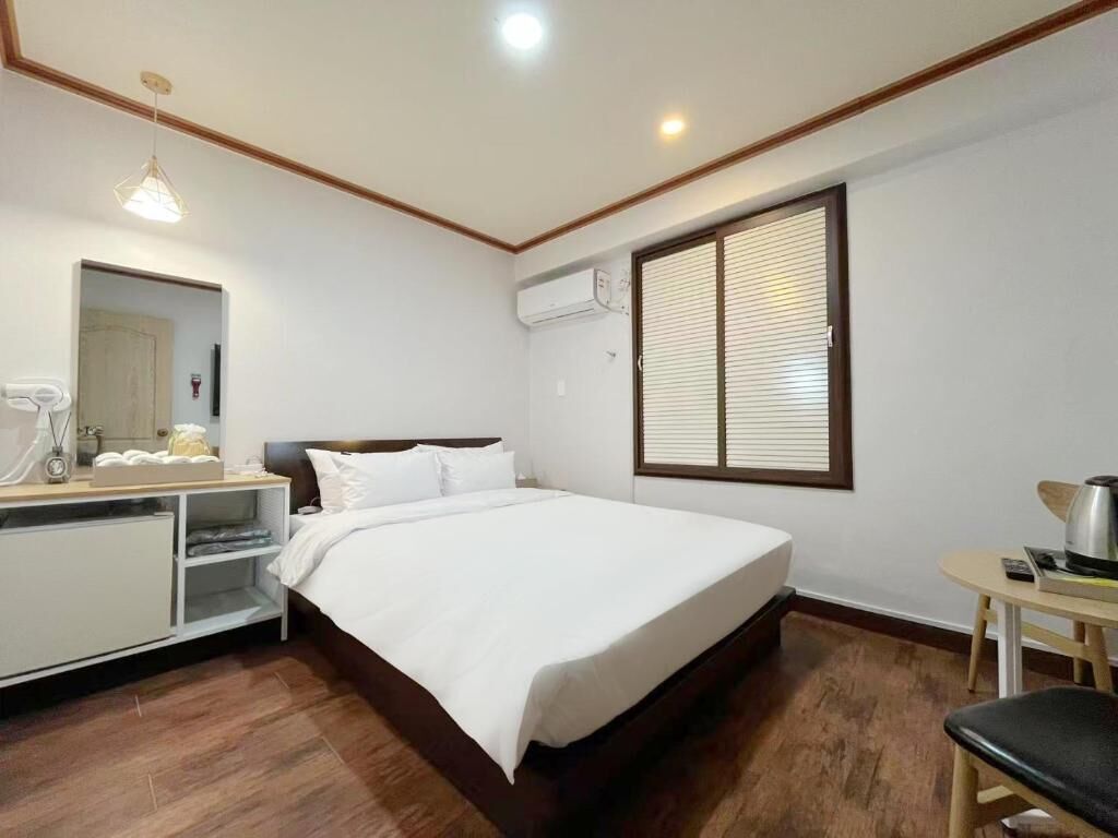 A hotel room with a bed, bedside table, mirror, and a window with blinds.