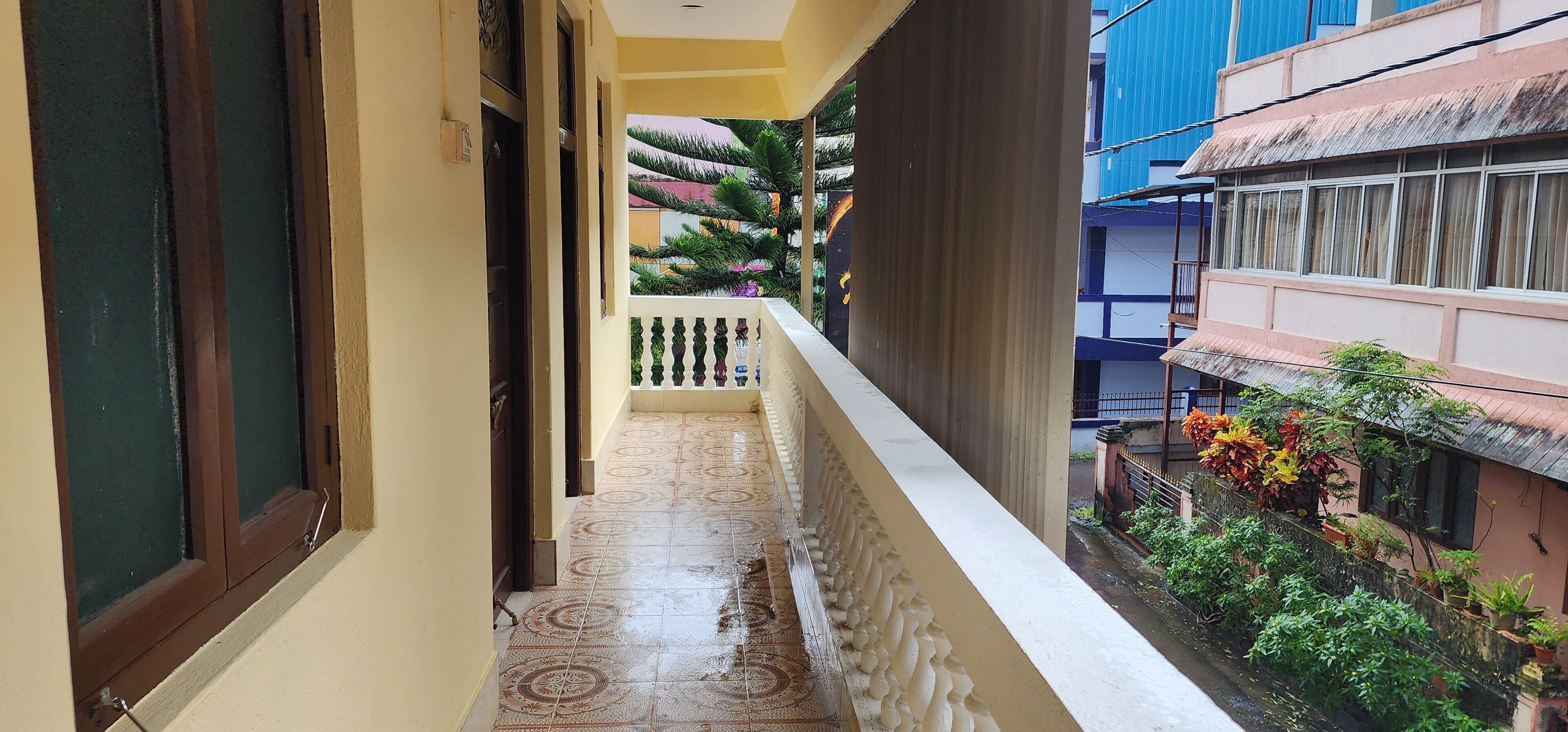 A narrow balcony with patterned floor tiles, a white balustrade, and a view of neighboring buildings and greenery.