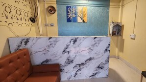 A reception area with a marble counter, a brown leather chair, a black sofa, and wall art. - Hotel Roy's (Port Blair)