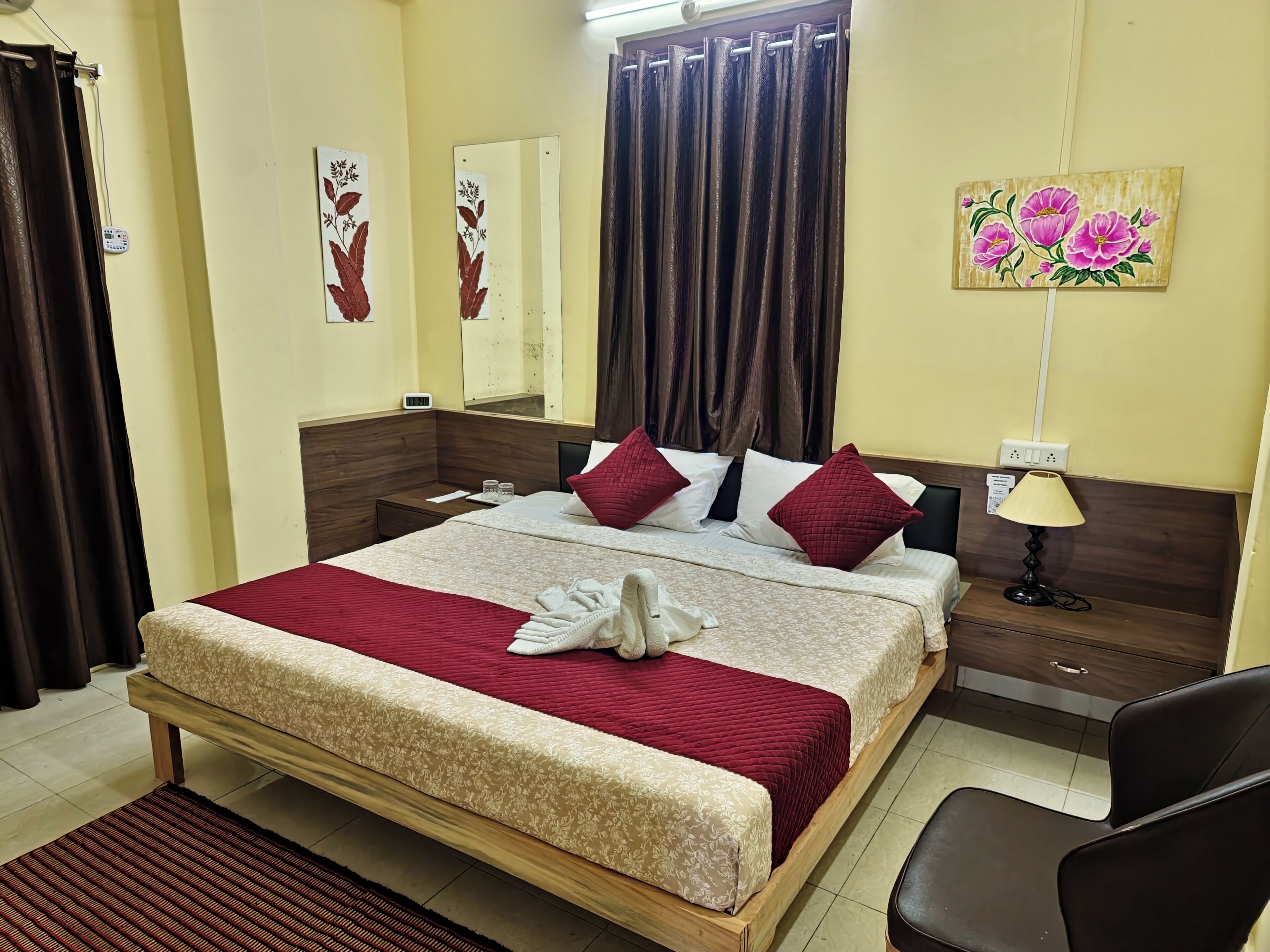 A hotel room with a bed, a bedside table, a lamp, a painting, and a window with curtains.