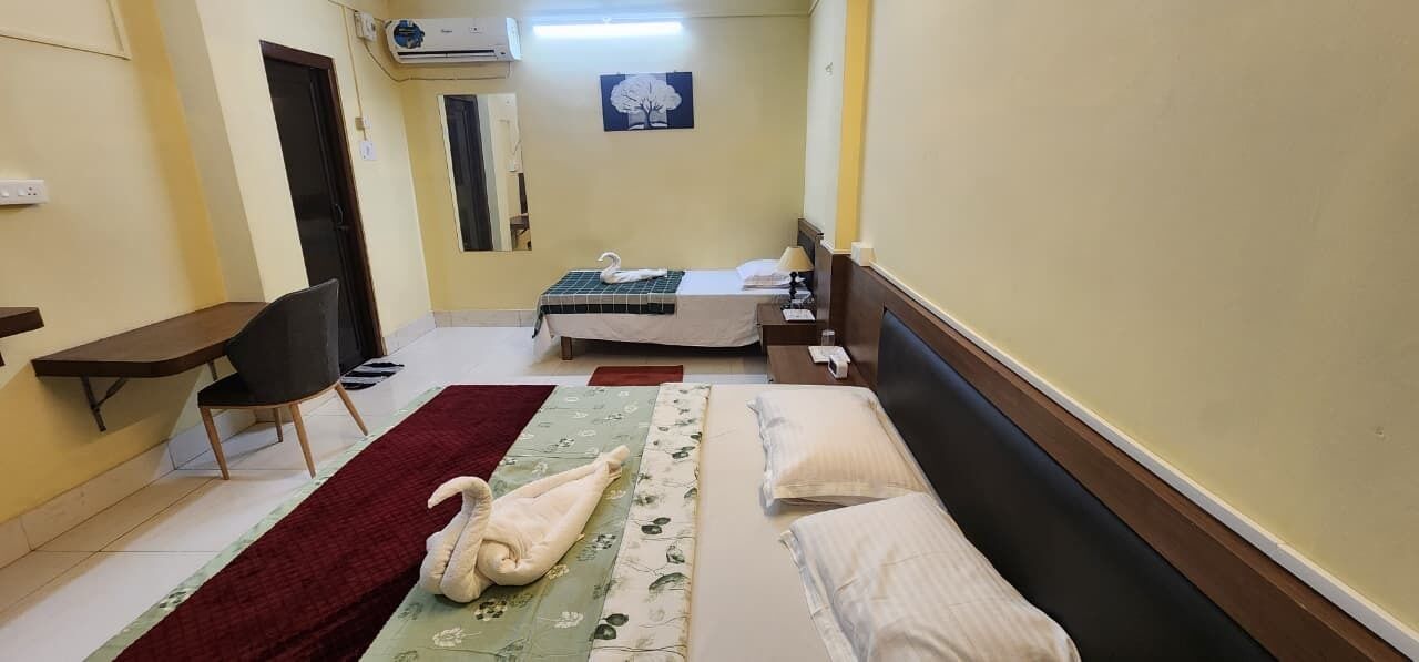 A hotel room with a bed, a desk, a chair, a red rug, and a wall-mounted air conditioner.
