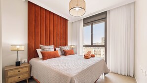Una camera da letto con un letto grande, un comodino, una lampada e vista sugli edifici attraverso la finestra.