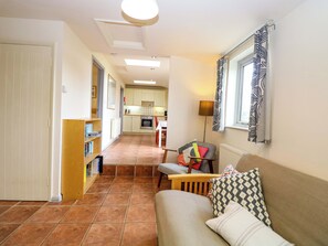 A hallway leading to a kitchen and living area with a sofa, a table, and a lamp. - Hollyhock (King's Lynn)