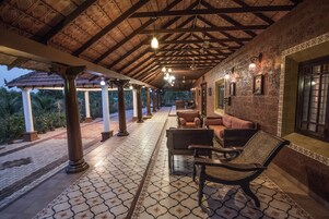 A covered outdoor seating area with patterned flooring, columns, and wall-mounted lights.