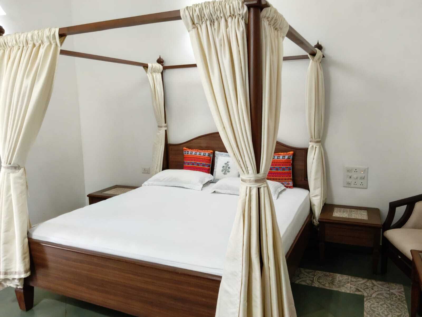 Una cama con dosel de madera y cortinas color crema.
