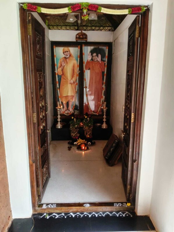 A shrine with two framed portraits, a small altar with offerings, and a bell above.