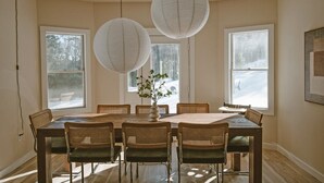 Uma sala de jantar com uma mesa grande, seis cadeiras, duas lanternas de papel suspensas e um vaso com folhagens.