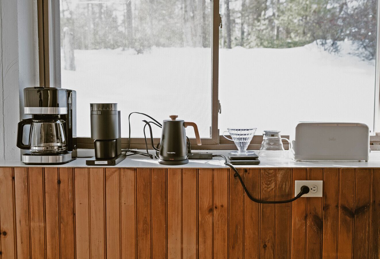 Un plan de travail de cuisine avec une machine à café, une bouilloire, un grille-pain et une carafe en verre.