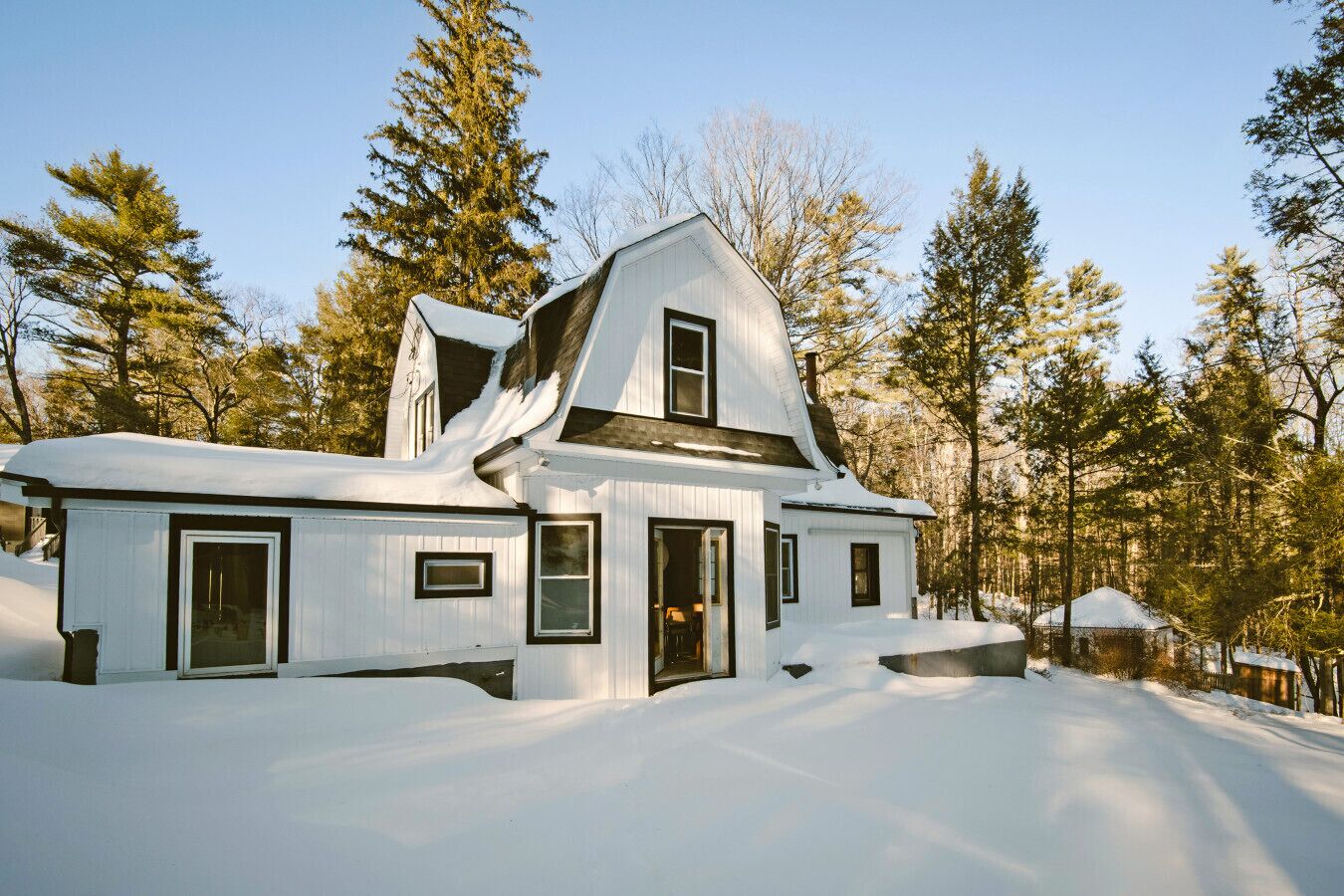 Une maison recouverte de neige, avec un toit à pignon, entourée d’arbres.