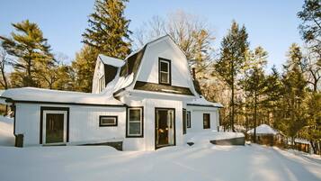 Une maison recouverte de neige, avec un toit à pignon, entourée d’arbres.