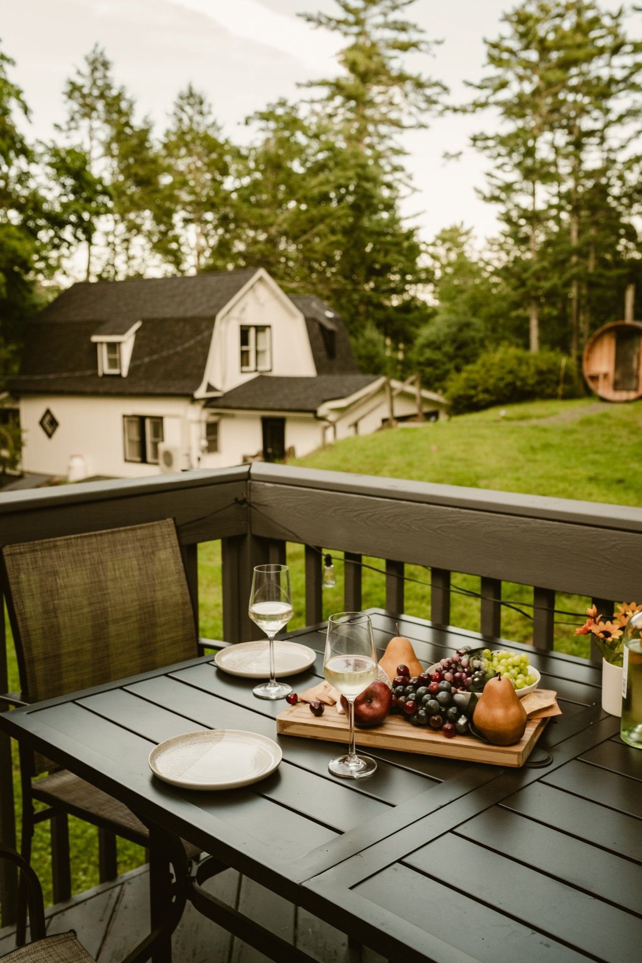 A wooden deck with a table set for a meal, featuring plates, glasses, and a fruit platter.