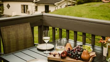 A wooden deck with a table set for a meal, featuring plates, glasses, and a fruit platter.