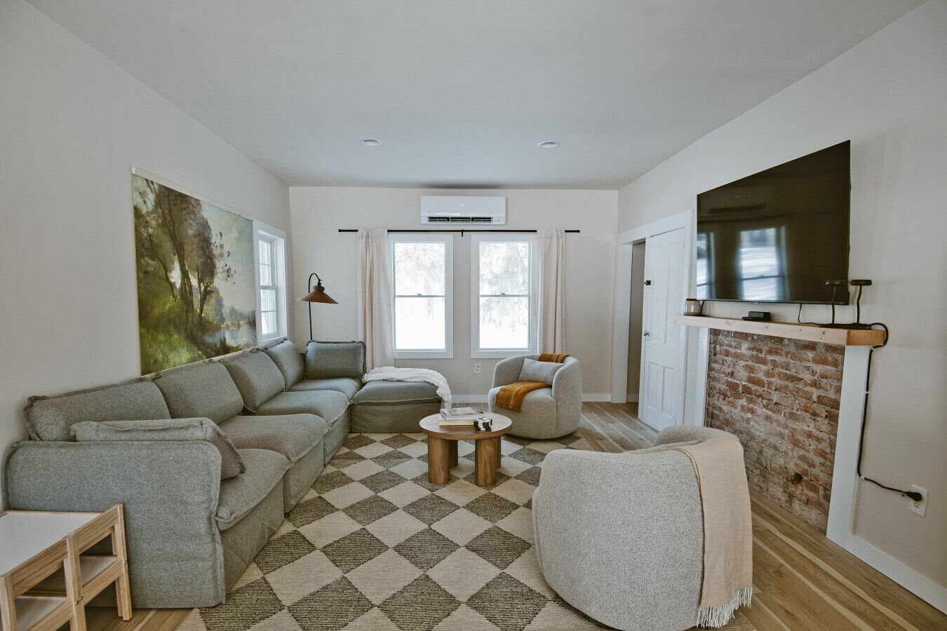 A living room with a sectional sofa, a round coffee table, a fireplace, and a large TV mounted on the wall.