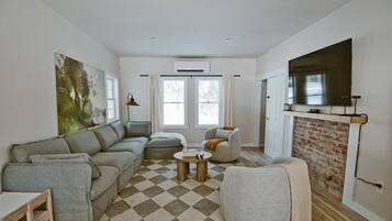 A living room with a sectional sofa, a round coffee table, a fireplace, and a large TV mounted on the wall.