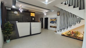 A reception area with a reception desk, a staircase, and a wall-mounted clock. - HAPPY HOTEL (Botad)