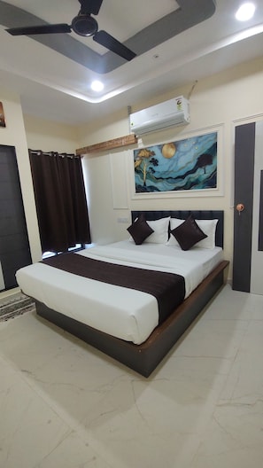 A bedroom with a bed, dark curtains, a ceiling fan, an air conditioning unit, and a painting on the wall. - HAPPY HOTEL (Botad)