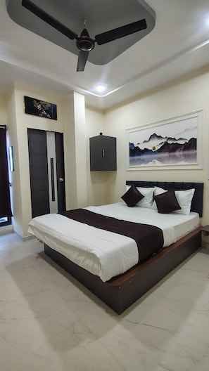A bedroom with a bed, a ceiling fan, a door, a cabinet, and a painting on the wall. - HAPPY HOTEL (Botad)
