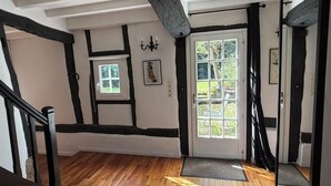 Ein Zimmer mit Holzboden, einer weißen Tür mit Glasfeldern, einer schwarz-weißen Wand mit einem Bild und einer Treppe mit schwarzen Geländern.