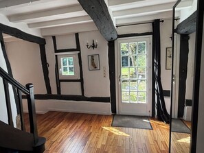 Una habitación con piso de madera, una puerta blanca con paneles de vidrio, una pared blanco y negro con un cuadro y una escalera con barandillas negras.