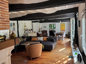 Una habitación con piso de madera, un sofá, una silla de mimbre, una mesa y una ventana.