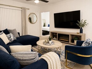 Ein Wohnzimmer mit einem dunkelblauen Sofa, einem runden Couchtisch und einem flachbildfernseher, der an der Wand montiert ist.