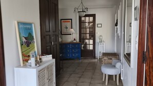 Un pasillo con piso de baldosas, un mueble blanco, un aparador azul, una mesita redonda pequeña y una puerta con panel de vidrio.