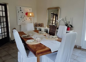 A dining room with a wooden table set for four, white chairs, a lamp, a mirror, and a decorative wall piece.