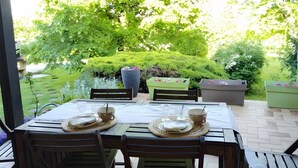 Un patio al aire libre con una mesa dispuesta para dos, rodeado de sillas y vistas a un jardín exuberante.