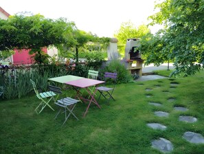 A garden patio with a table and chairs, surrounded by lush greenery and a stone pathway. - Les Chambres D’Anel - La Besbre: Guest Rooms with Pool, Terrace and Wi-Fi (Saint-Pourçain-sur-Besbre)
